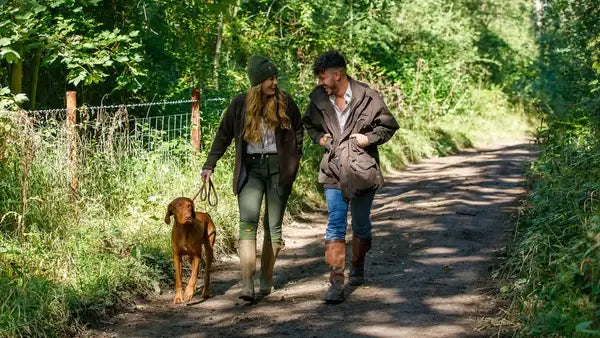 Two people walking a dog on a path through a forest